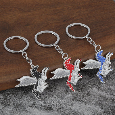Three silver-tone winged horse keychains in black, red, and blue on a wood surface.