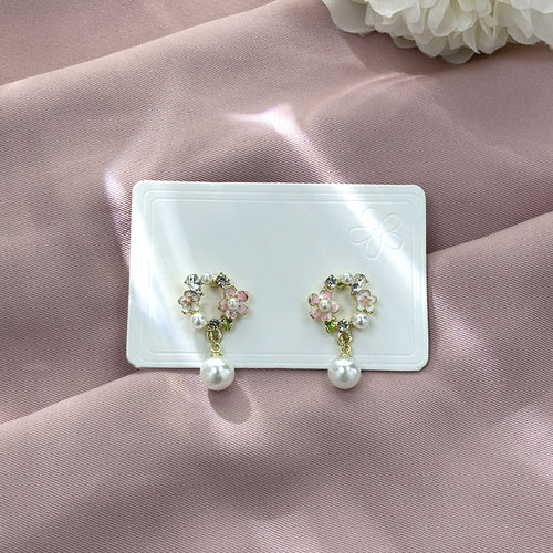 Pink enamel flower wreath pearl drop earrings on white card over pink satin