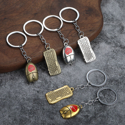 Silver-tone, bronze-tone, and gold-tone mouse and keyboard keychains arranged on wood and gray fabric.