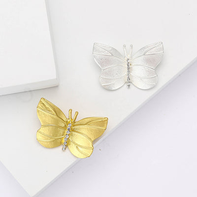 Gold and silver matte butterfly brooches on white blocks