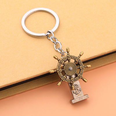 Antique brass-tone ship wheel keychain resting against the edge of a tan book.
