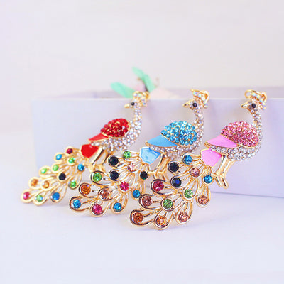 Three gold-tone peacock ornaments in red, blue, and pink with multicolor stone tails.
