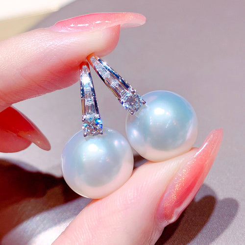 Close-up of crystal-set tapered hoops with iridescent faux pearl drops