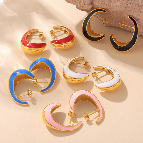 Five color pairs of crescent enamel earrings on sand with rock
