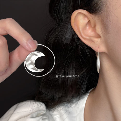 Hammered sun-and-crescent hoop earrings shown worn on an ear.
