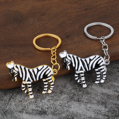Two black-and-white zebra keychains with silver-tone and gold-tone hardware on a wood surface.