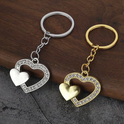 Gold-tone and silver-tone double heart keychains displayed on a wooden surface.