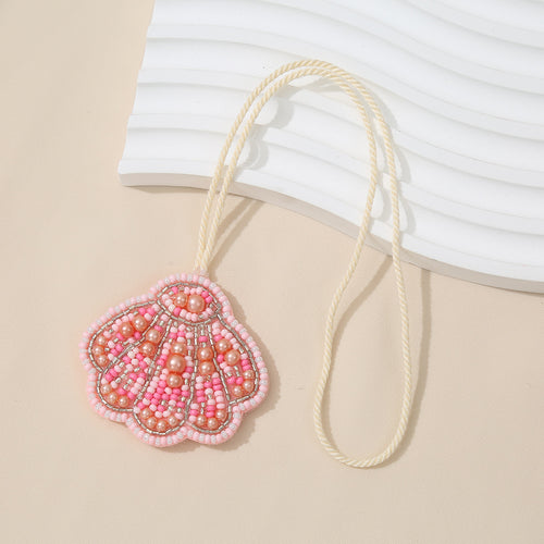 Pink and coral beaded pearl seashell charm pendant hanging from a cream cord
