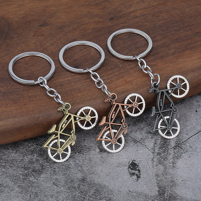 Three bicycle-shaped metal charms in brass, copper, and dark silver tones attached to split rings.