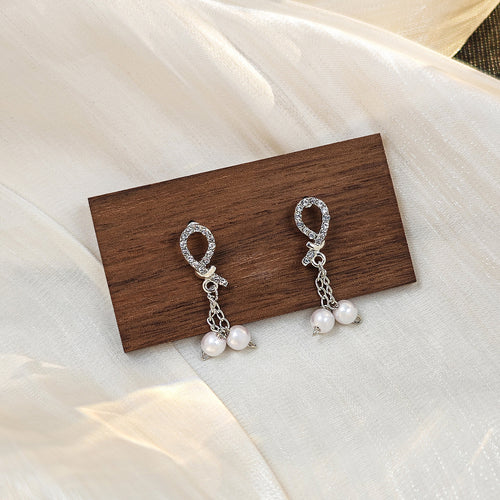 Silver rhinestone bow studs with pearl chains on wood block