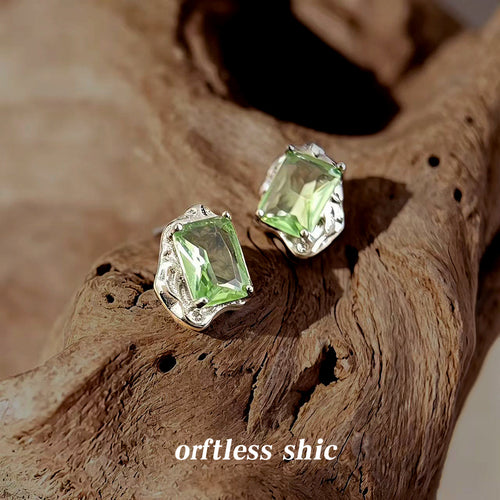 Silver-tone pale green rectangular stone stud earrings on natural wood.