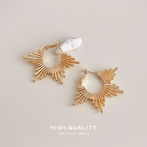 Gold sunburst radial bar hoop pair beside white stone