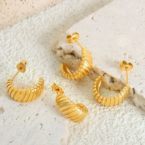 Four gold ribbed crescent stud earrings on textured stone surface