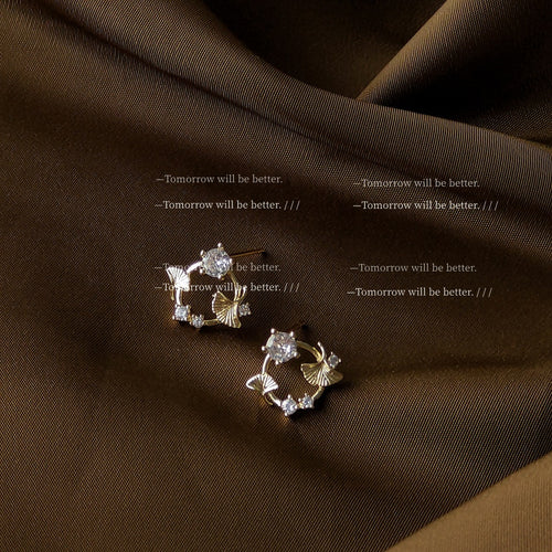 Gold ginkgo leaf circle studs on brown satin fabric