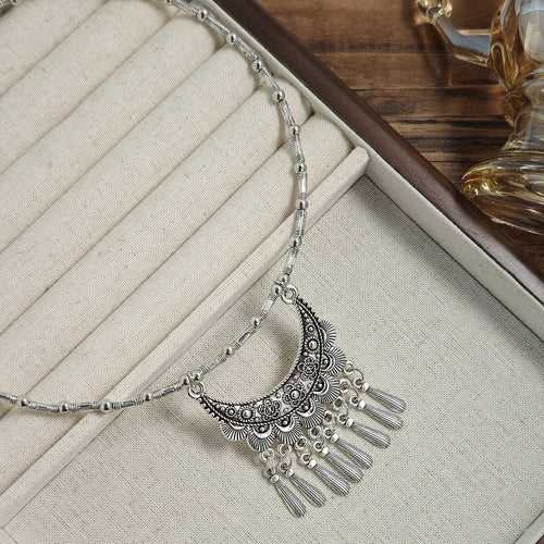 Silver crescent moon tassel fringe choker on beige jewelry tray close-up