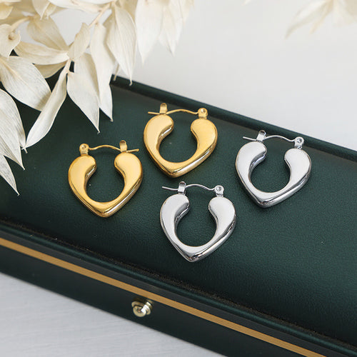Gold and steel heart teardrop hoops on green jewelry tray