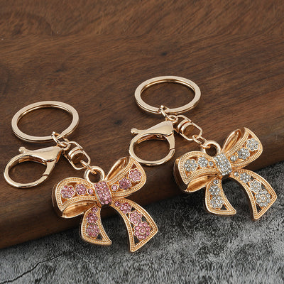 Two gold-tone bow keychains with white and pink rhinestone flower details.