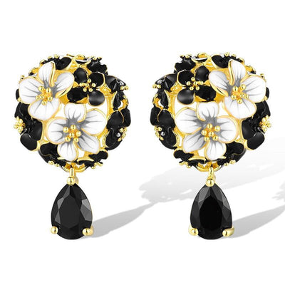 Gold tone floral drop earrings with black and white petals, product displayed in a styled close-up