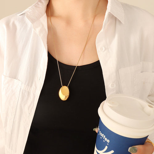 Gold oval pebble pendant worn with white shirt and coffee cup