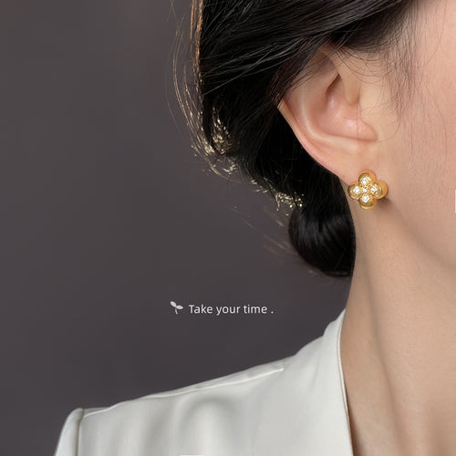 Gold four leaf clover stud worn on ear dark hair profile