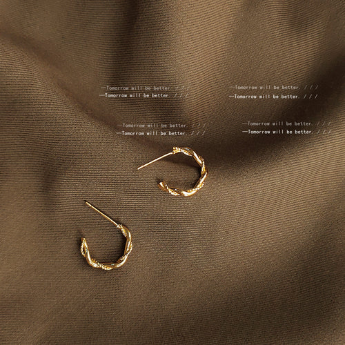 Gold twisted open C hoop studs on brown draped fabric