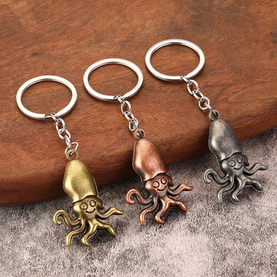 Three squid keychains in bronze, copper, and silver tones rest on a wooden surface.