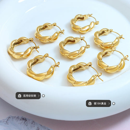 Several gold twisted hoops on white dish with material labels