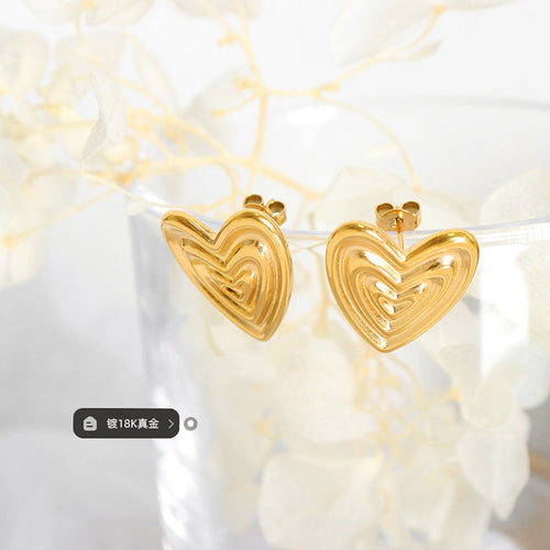 Pair of gold ribbed heart studs hanging on glass with plating tag