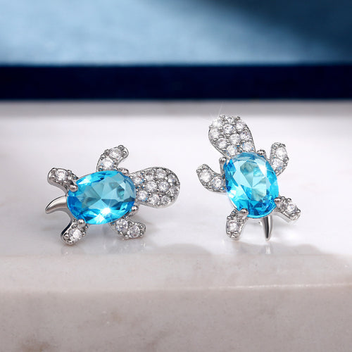 Pair of silver turtle studs with aqua oval shells on white marble