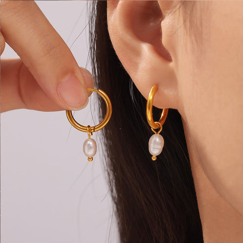 Gold pearl huggie hoop earring worn and held near ear