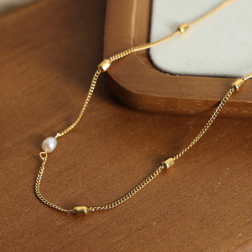 Close-up gold chain white pearl and barrel beads on wooden surface