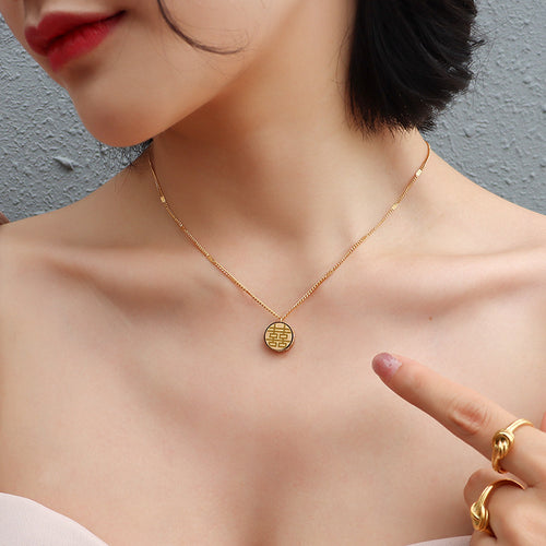 Model wearing gold double happiness coin pendant necklace pointing at pendant