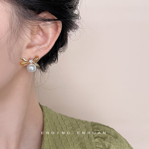Gold bow pearl stud worn on ear with green top