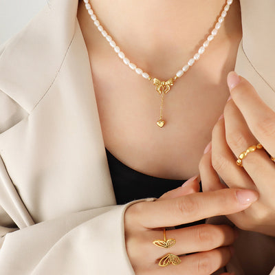 Model wearing pearl bead necklace with gold bow and heart drop pendant