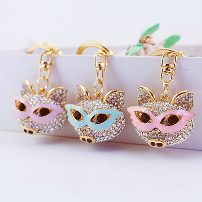 Three jeweled pig-face charms with pink, pale blue, and light purple eye masks hang from gold-tone clasps.