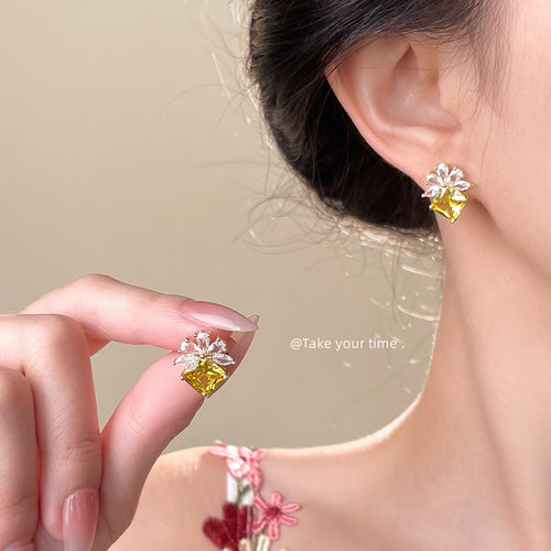 Model wearing yellow gem flower stud while holding matching earring