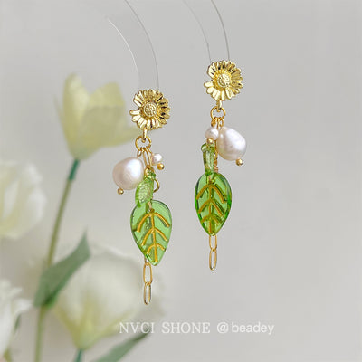 Gold daisy pearl green leaf chain drop earrings hanging against soft background