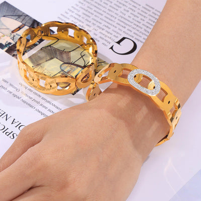 Gold chain link rhinestone cuff bangle worn on wrist over magazine