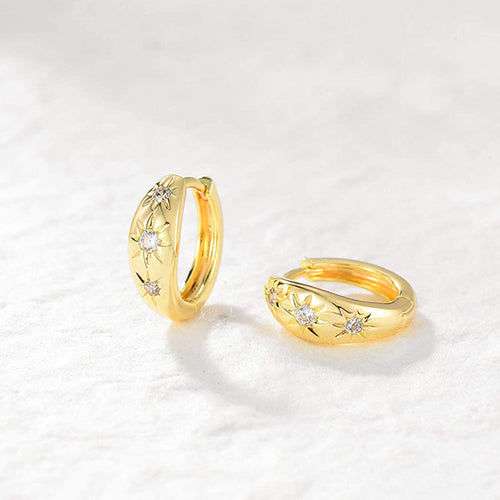 Gold huggie hoops with three star clear stones on soft white fabric