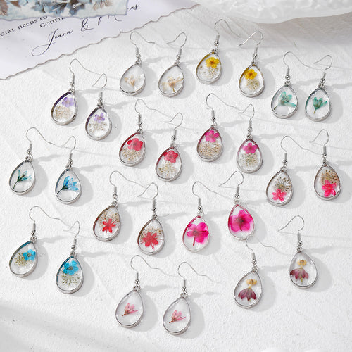 Assortment of teardrop pressed flower resin earrings in many colors on white surface