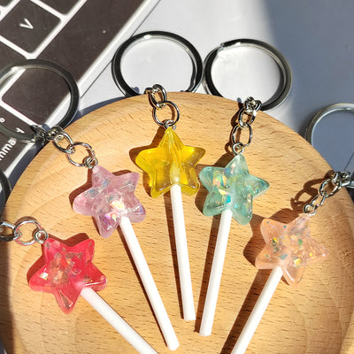 Five resin glitter star lollipop keychains in mixed colors on wood tray