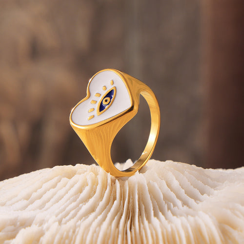 Gold heart evil eye signet ring standing on white coral surface