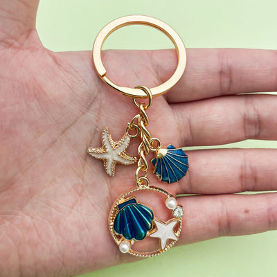 Image 1 showing a person holding a gold keychain with seas and starfish charms.