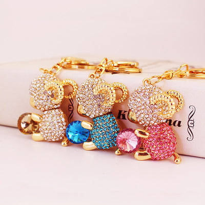 Three gold-tone ram keychains with white, blue, and pink rhinestone bodies.