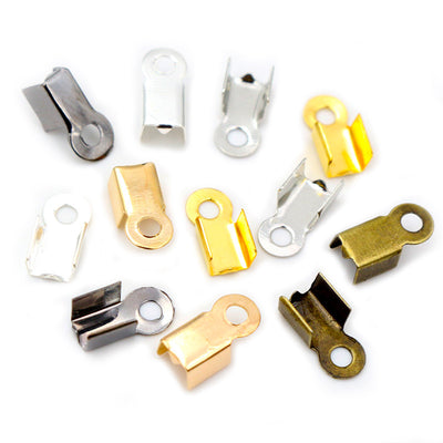 Assorted fold-over cord end crimps in mixed metal finishes arranged together on a plain background