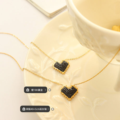Two gold black crystal heart necklaces on saucer with labels