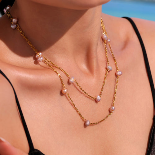 Close-up of two gold pearl station necklaces on collarbone outdoors