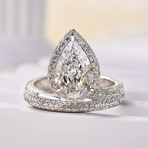 Pear halo crystal ring resting on white surface showing pave wrap band