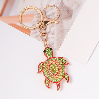 Green rhinestone turtle keychain with red enamel on white surface