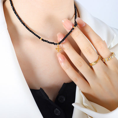 Model wearing black beaded necklace with gold cross pendant